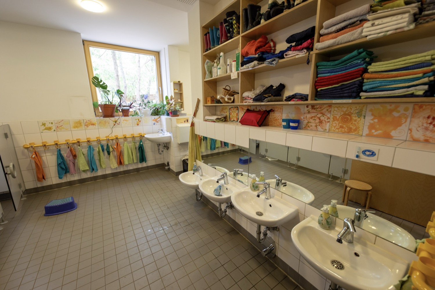 Kinder-Waschraum mit niedrigen Waschbecken, Spiegeln und bunten Handtüchern an der Wand